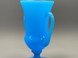 a blue glass cup with a handle sitting on a table