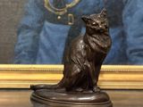 une statue représentant un chat assis sur une table, à côté d'un tableau