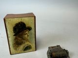 une petite boîte sur laquelle figure l'image d'une femme coiffée d'un chapeau, à côté d'une boucle de ceinture
