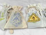 trois petits sacs à cordon ornés de symboles maçonniques, posés sur un lit