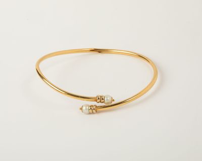 a gold bang bracelet with two pearls on it