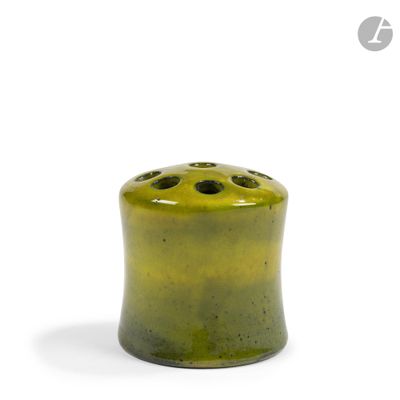 un vase vert percé de trous posé sur une surface blanche