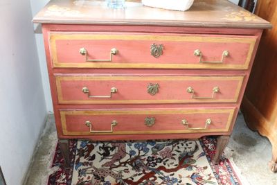 a pink dresser with gold hardware and a white vase on top of it