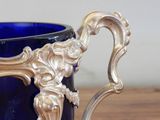 a blue glass cup with a silver handle on a wooden table