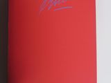someone is holding a book with a red cover and a blue signature
