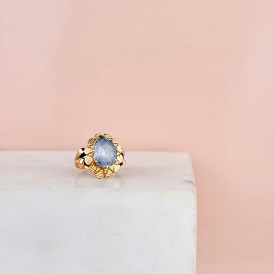 une bague en or sertie d'une pierre bleue, posée sur un bloc de marbre