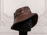 chapeau de pêcheur en cuir marron posé sur une tête de mannequin devant un mur blanc