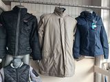 many coats and jackets hanging on a rack in a room