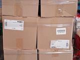 plusieurs cartons empilés sur une palette dans un entrepôt, avec une personne à l'arrière-plan