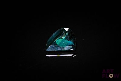 a green tourmaline in a triangular cut on a black surface