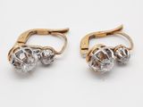 deux paires de boucles d'oreilles en or et en cristal posées sur un fond blanc