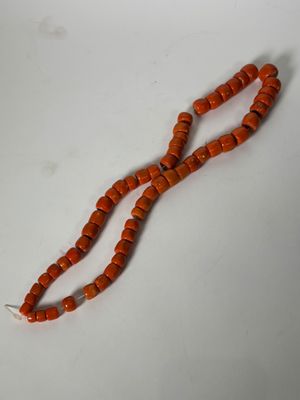 un gros plan d'un collier de perles orange posé sur une surface blanche