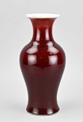 un vase rouge avec un couvercle blanc posé sur une surface blanche