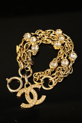 a close up of a gold chain bracelet with a chanel charm