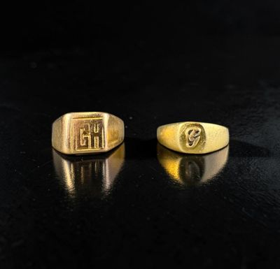 two gold rings with initials on them on a black surface