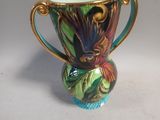 a colorful vase with a gold handle on a white table