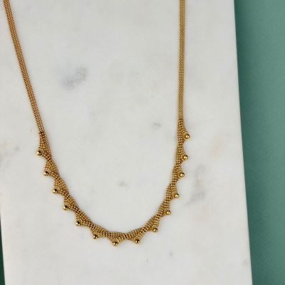 un collier plaqué or posé sur une dalle de marbre