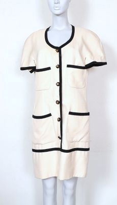 une robe blanche avec des bordures et des boutons noirs sur un mannequin