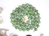 a green bead necklace and other jewelry on a white surface