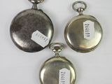 three silver pocket watches with tags on them sitting on a white surface