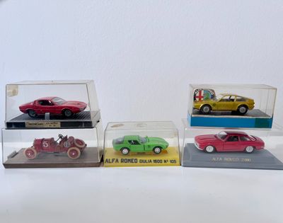 Quatre modèles réduits de voitures différents sont exposés dans une vitrine posée sur un socle blanc.