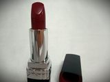 red lipstick on a white surface next to a black bottle