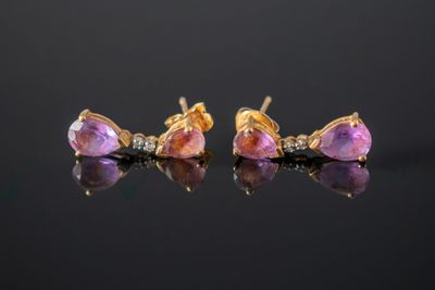 une paire de boucles d'oreilles en saphir rose et diamants posées sur un fond noir
