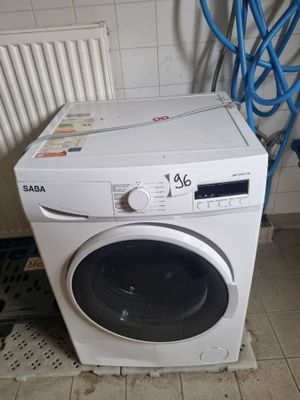 une machine à laver blanche posée sur un sol carrelé, à côté de tuyaux bleus