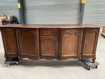 un grand buffet en bois monté sur roulettes, dans un entrepôt