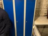 un homme debout à côté d'un casier bleu dans une pièce