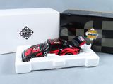 une petite voiture rouge et noire dans une boîte blanche, à côté d'une boîte noire et blanche