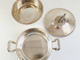 two silver plated dishes with handles and lids on a white surface