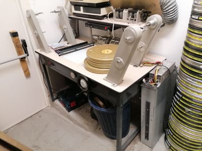 une table sur laquelle se trouve un disque, dans une pièce où s'entassent de nombreuses piles de disques