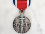 médaille d'argent ornée d'un ruban rouge, blanc et bleu posée sur une surface en marbre