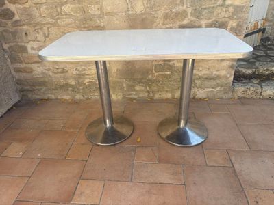 a white table with two silver legs on a brick floor
