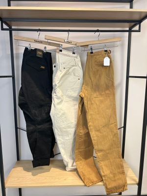 trois paires de pantalons suspendues à un portant dans un magasin de vêtements
