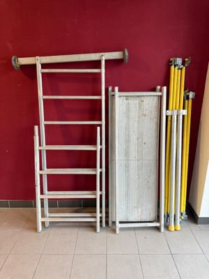 une échelle appuyée contre un mur rouge, à côté d'une pile d'échelles