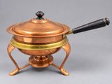 une vieille casserole en cuivre avec une poignée noire, posée sur un support