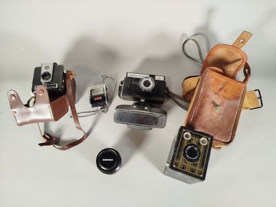 Plusieurs anciens appareils photo sont posés sur une surface blanche, accompagnés d'un étui en cuir.