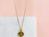 un collier composé d'une médaille en or suspendue à une chaîne en or, sur fond rose