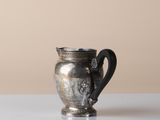 a silver cup sitting on a table with a brown wall in the background