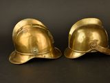 pair of brass fire helmets on a black background