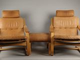 deux fauteuils inclinables en cuir marron et un repose-pieds dans une pièce avec un rideau rouge