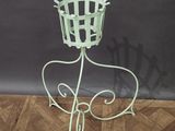 green metal plant stand with a basket on top of it on a wooden floor