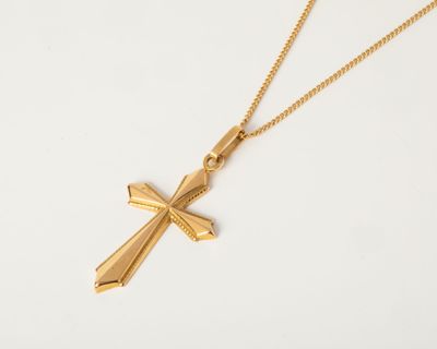un pendentif en forme de croix en or, suspendu à une chaîne en or, sur fond blanc