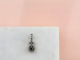 un gros plan d'un petit pendentif en forme de losange vert et blanc posé sur une surface en marbre blanc