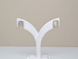 une paire de boucles d'oreilles « oplite » posées sur un socle blanc, sur une table