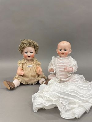 deux poupées en porcelaine assises l'une à côté de l'autre sur une surface grise