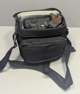 a black camera bag with a camera in it on a white table