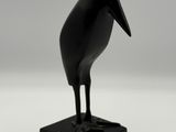 statue d'un oiseau noir posée sur un socle noir, sur fond blanc